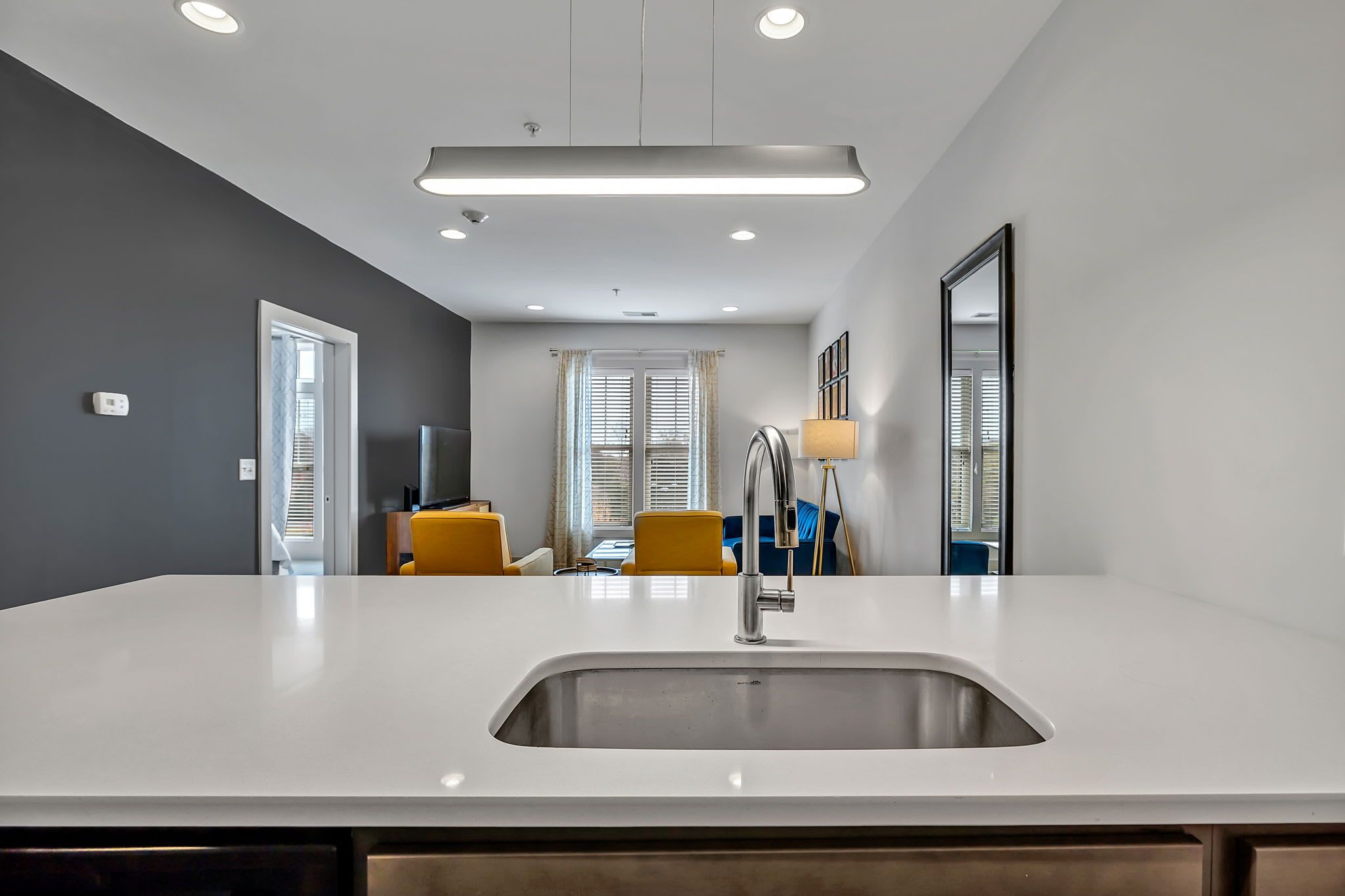 A modern kitchen with a white countertop, stainless steel sink, and overhead lighting.