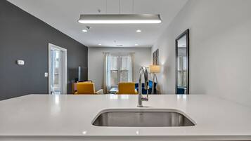 A modern kitchen with a white countertop, stainless steel sink, and overhead lighting.