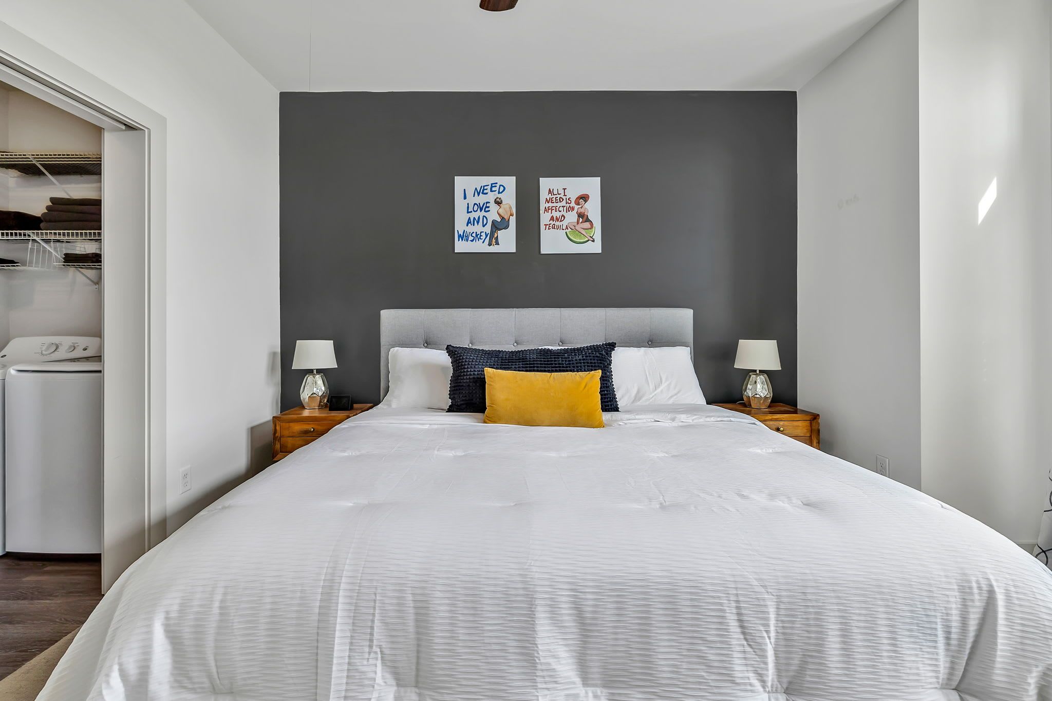 A modern bedroom with a large bed, two bedside tables with lamps, a grey headboard, and a wardrobe with a mirror.
