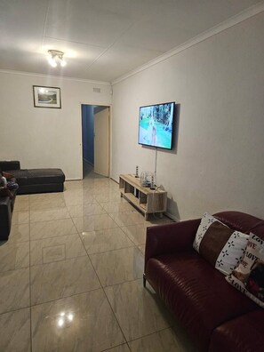 Een woonkamer met een aan de muur bevestigde televisie, een bank, een salontafel en een deur naar een andere kamer.