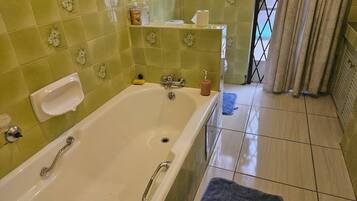 A bathroom with a bathtub, a toilet, and a sink. There is a towel rack and a shelf with toiletries.
