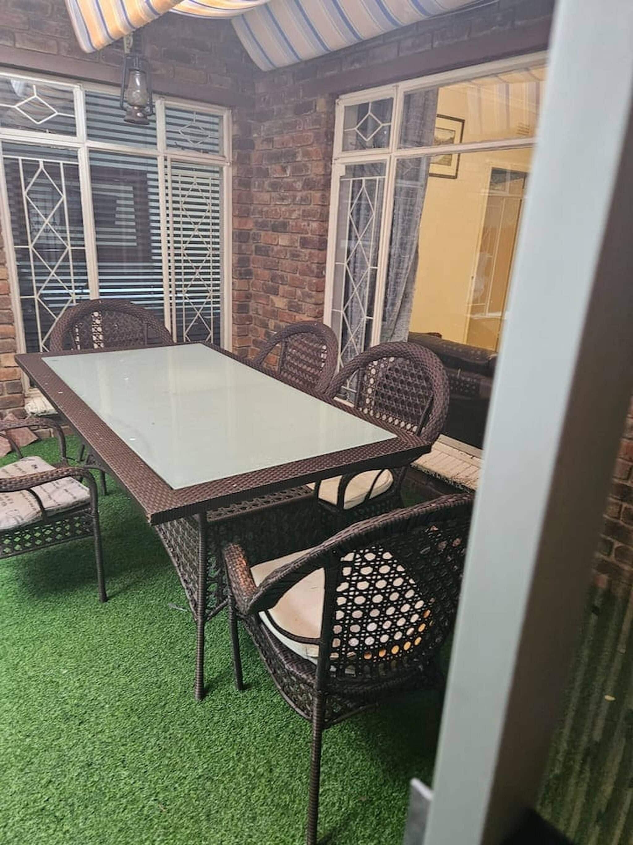 A patio area with a glass-top table, wicker chairs, and a brick wall.