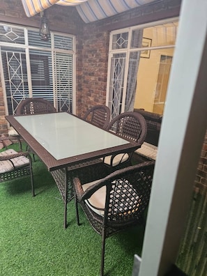 A patio area with a glass-top table, wicker chairs, and a brick wall. - Spacious 3-bedroom House Rental in Randburg, South Africa (Johannesburg)