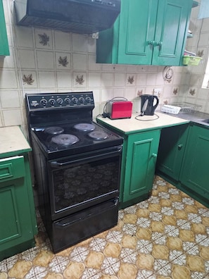 A kitchen with a black stove, green cabinets, a red toaster, and patterned floor tiles. - Spacious 3-bedroom House Rental in Randburg, South Africa (Johannesburg)