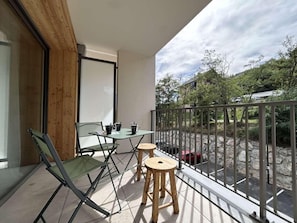 A balcony with a table and chairs, a glass chair, and a view of a stone wall and greenery. - 300m from ski slopes, 2nd floor, terrace, tv, ski locker, 58m², Serre Chevalier (Briançon)