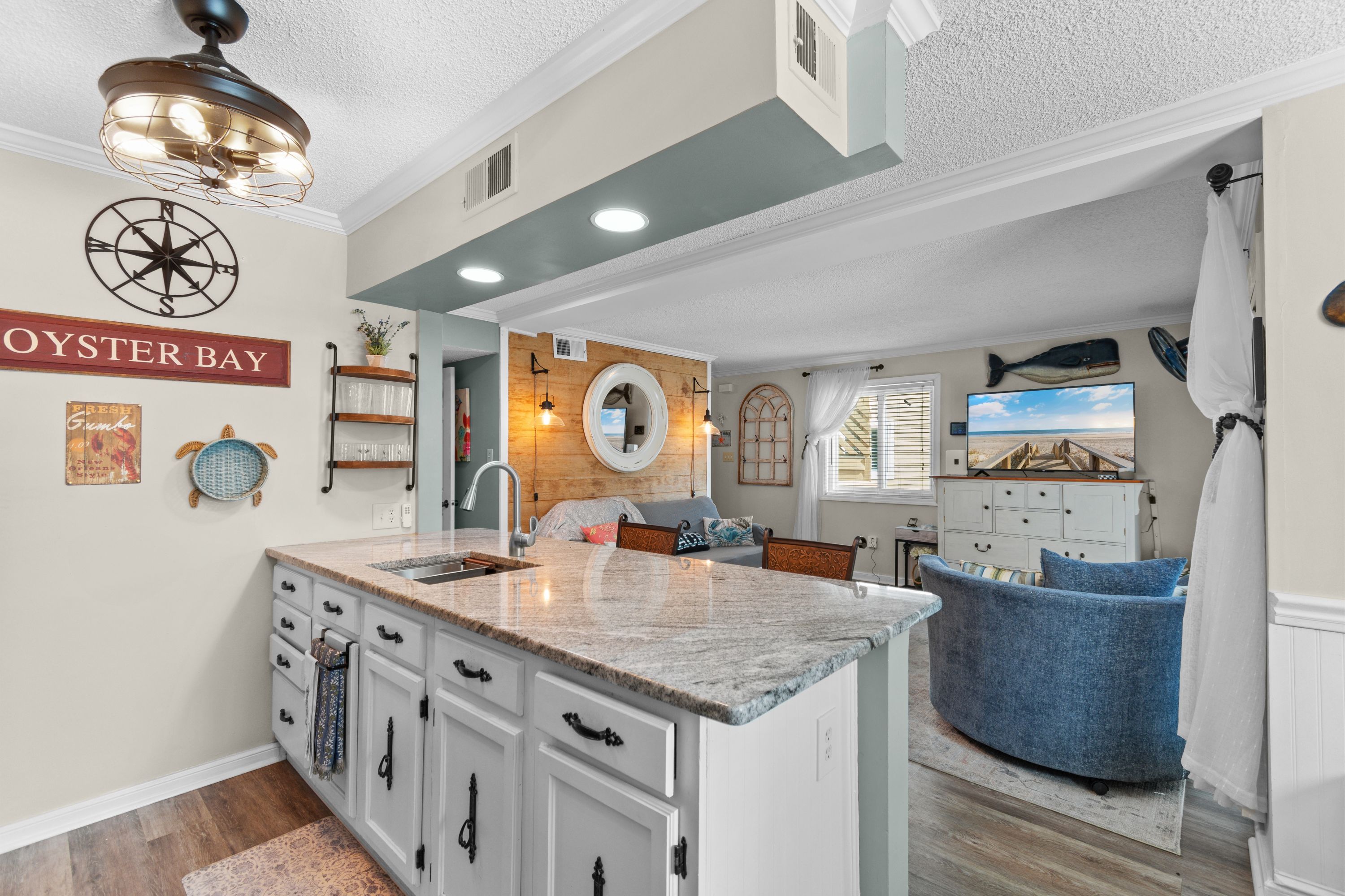 A kitchen with a central island, a dining area with a blue chair, and a wall-mounted TV.