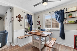 A dining area with a wooden table and benches, a ceiling fan, and a window with curtains. - Porch & Palms - ground-floor 2BR, pool, near beach (North Myrtle Beach)