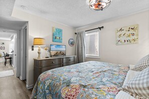 Une chambre à coucher avec un lit, une commode, des œuvres d’art et une vue sur la plage.