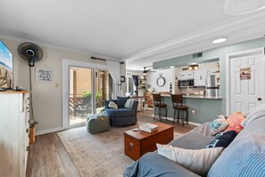 A living room with a sofa, a coffee table, and a dining area with chairs. There is a kitchen with a refrigerator and a microwave. - Porch & Palms - ground-floor 2BR, pool, near beach (North Myrtle Beach)