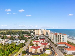 A coastal cityscape with a prominent hotel featuring a red-roofed building, a beachfront, and a clear view of the ocean. - Porch & Palms - ground-floor 2BR, pool, near beach (North Myrtle Beach)