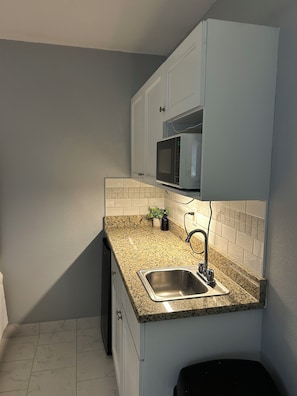 Cocina compacta con encimera de granito, pileta de acero inoxidable y microondas.