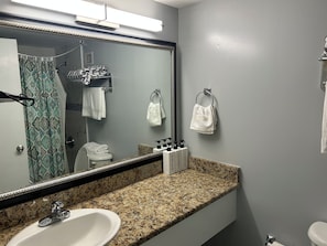 Un baño con encimera de granito, un lavabo blanco, un espejo grande y un perchero con varias toallas.