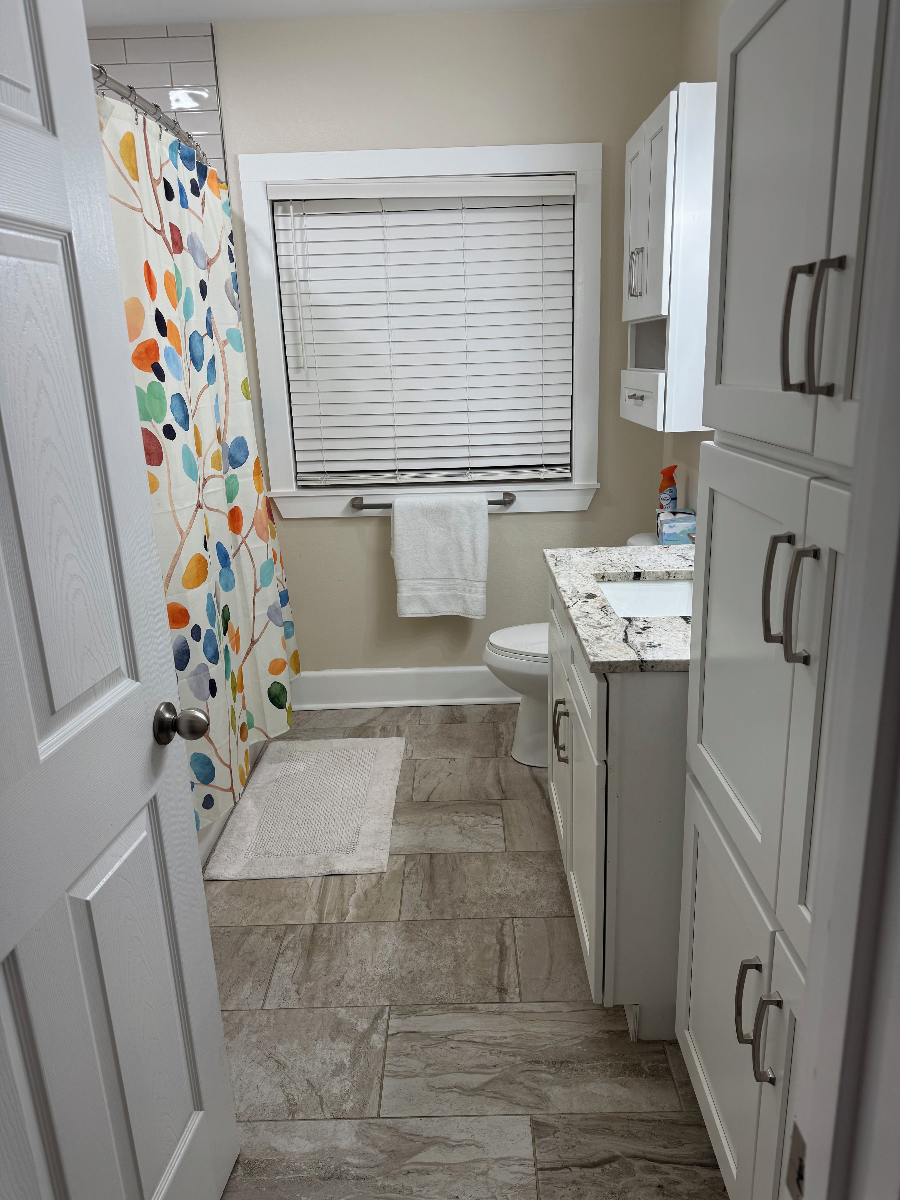A bathroom with a shower curtain, a toilet, a sink, and cabinets.