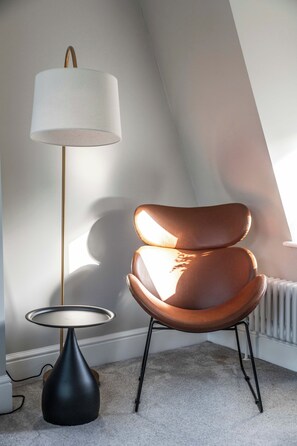 Ein modernes Zimmer mit schrägen Wänden, einem braunen Ledersessel, einer Stehlampe und einer Heizung.