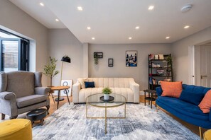 A living room with a sofa, armchair, coffee table, and bookshelf. - Family Home by Battersea Park | 4 Beds + Garden (Greater London)