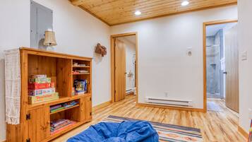 A room with a wooden ceiling, a bookshelf, a blue bean bag, and a shower area.