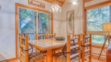 A dining area with a wooden table and chairs, large windows with views of trees, and a chandelier.