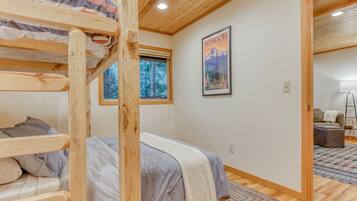 A room with a bunk bed, a framed poster, a window with a view of trees, and a wooden floor.