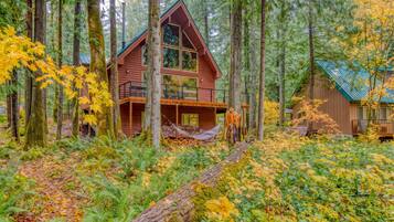 Une cabane dotée d’un balcon, entourée d’une forêt aux couleurs automnales.