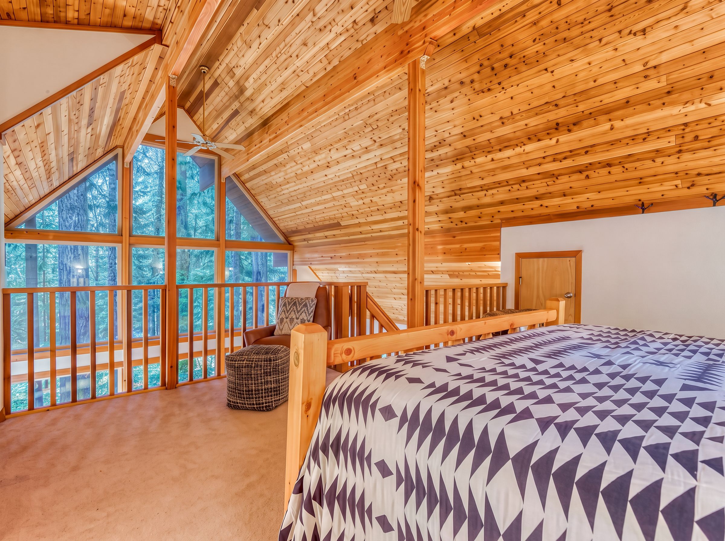 A bedroom with a sloped ceiling, large windows, a bed, and a wooden headboard.