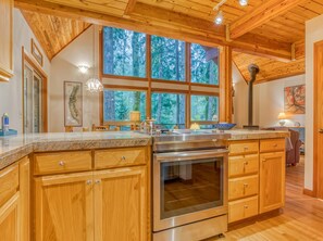 A kitchen with wooden cabinets, a stainless steel oven, and a large window with a forest view.