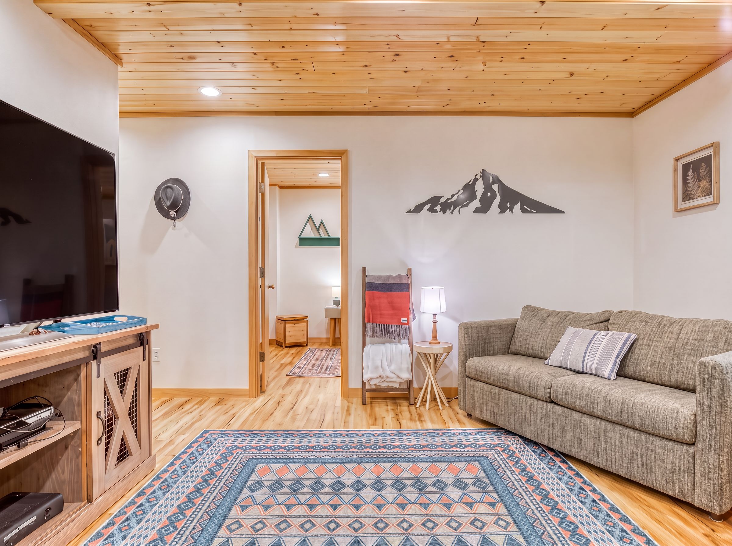 A cozy living room with a wooden ceiling, a sofa, a TV, and a patterned rug.