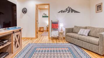 A cozy living room with a wooden ceiling, a sofa, a TV, and a patterned rug.