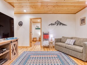 A cozy living room with a wooden ceiling, a sofa, a TV, and a patterned rug.