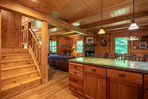 A wooden cabin interior with a staircase, a fireplace, a dining area, and a kitchen with wooden cabinets. - Camp Shanahan - Boat Access only camp (Webb)