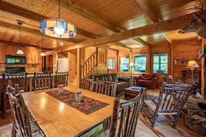 A rustic cabin interior with a wooden dining table, chairs, a fireplace, and a large window. - Camp Shanahan - Boat Access only camp (Webb)