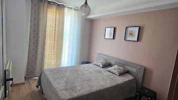 A bedroom with a bed, a bedside table, a radiator, and a window with curtains.