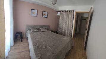 Quarto com cama, duas almofadas, cabeceira, mesa de cabeceira, luminária suspensa, porta e cortina.