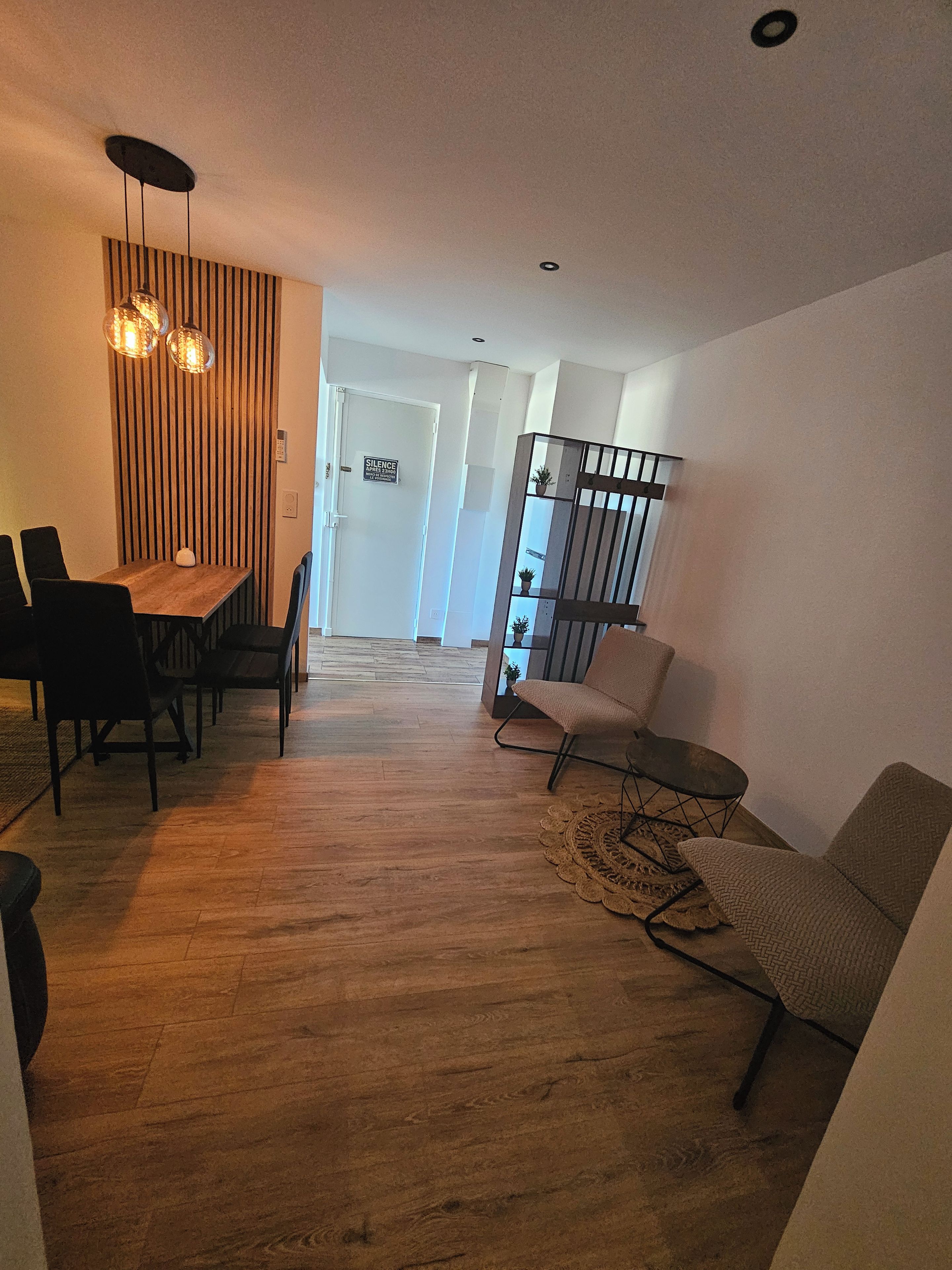 A modern living room with a wooden floor, a dining area with a table and chairs, and a staircase leading to another level.