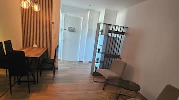 A modern living room with a wooden floor, a dining area with a table and chairs, and a staircase leading to another level.