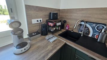 A kitchen with a coffee maker, a kettle, a sink, and a coffee-themed mat.