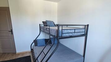 A bunk bed with a metal frame, a grey mattress, and a black headboard. There is a black rug on the floor and a door to the left.