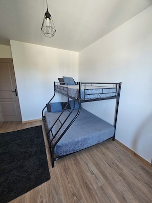 A bunk bed with a metal frame, a grey mattress, and a black headboard. There is a black rug on the floor and a door to the left. - Comfortable apartment 5 minutes from the train station (Perpignan)