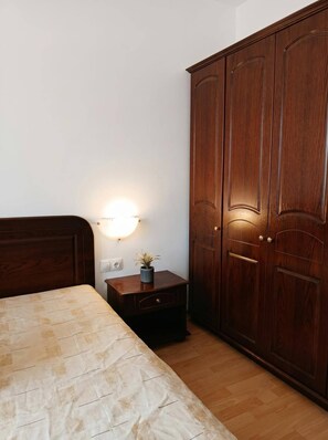A bedroom with a wooden wardrobe, a bedside table with a lamp, and a bed with a patterned bedspread. - South Facing Balcony 1 BR (Bansko)