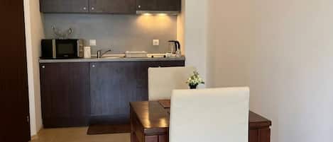 Cocina compacta con armarios oscuros, microondas y un pequeño comedor con mesa y dos sillas.