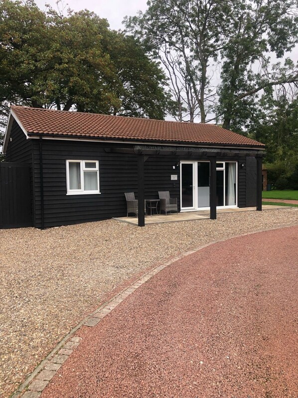 A black building with a tiled roof, a covered patio area, and a gravel driveway.