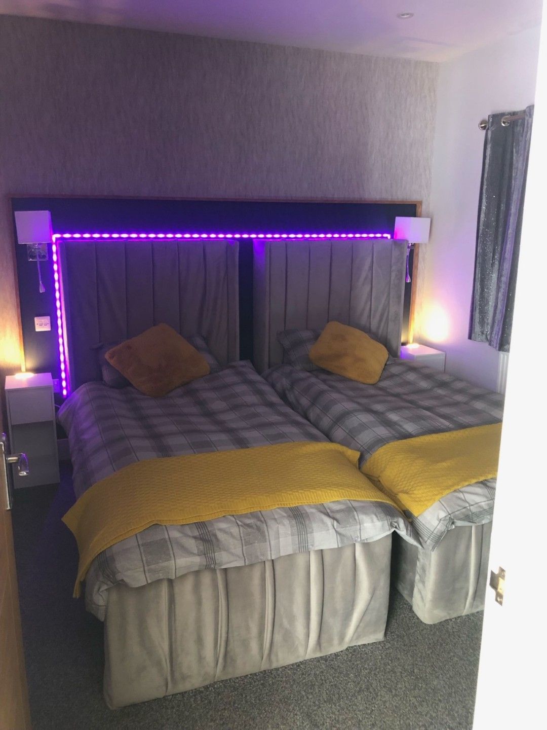 A double bed with a headboard featuring LED lights, two bedside tables, and a window with curtains.