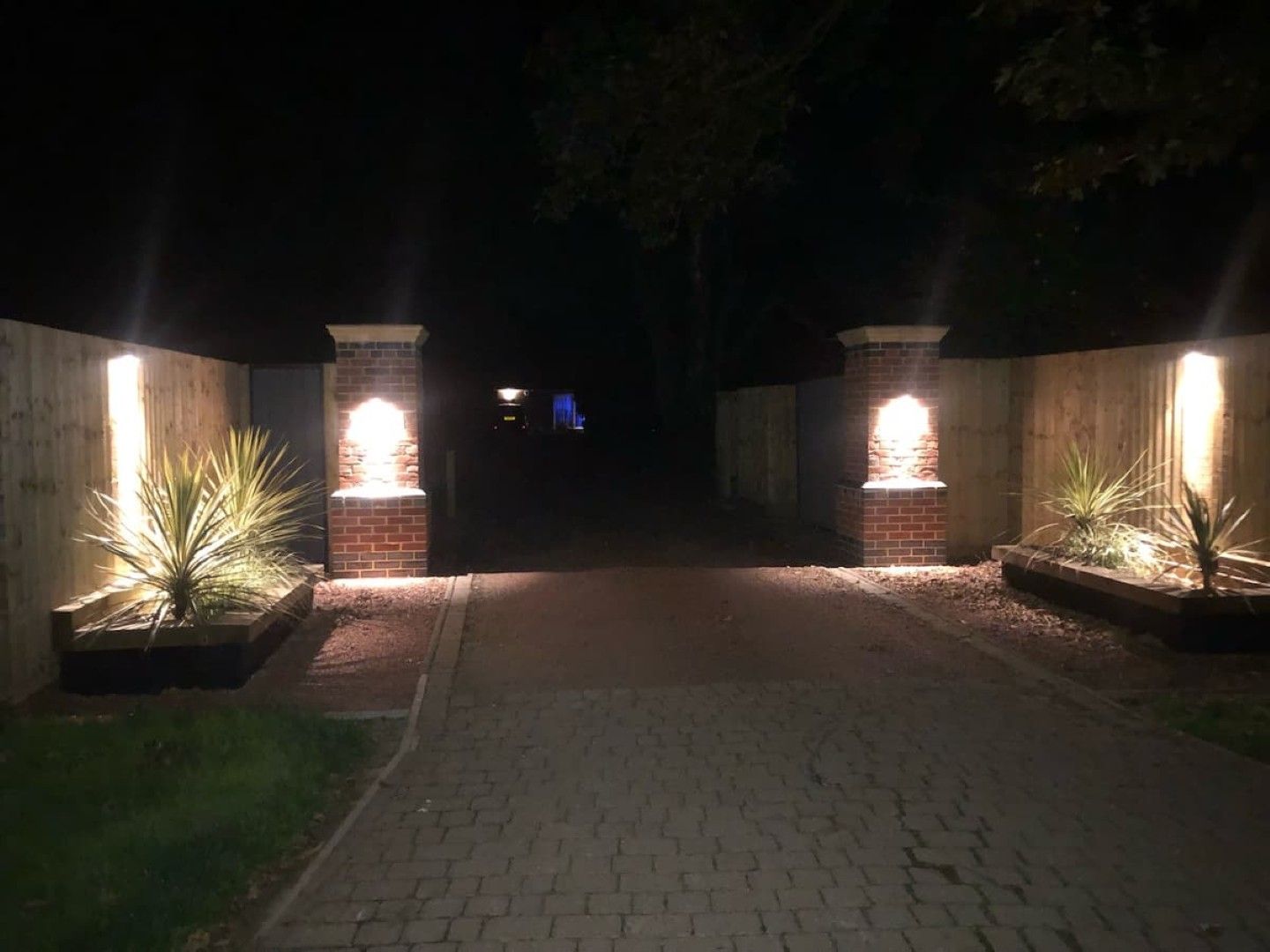 A pathway leading to a building with brick pillars and illuminated lights.