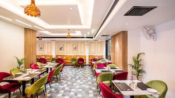 Een restaurant met een schakeerd motief op de vloer, meerdere eettafels met stoelen en hanglampen.