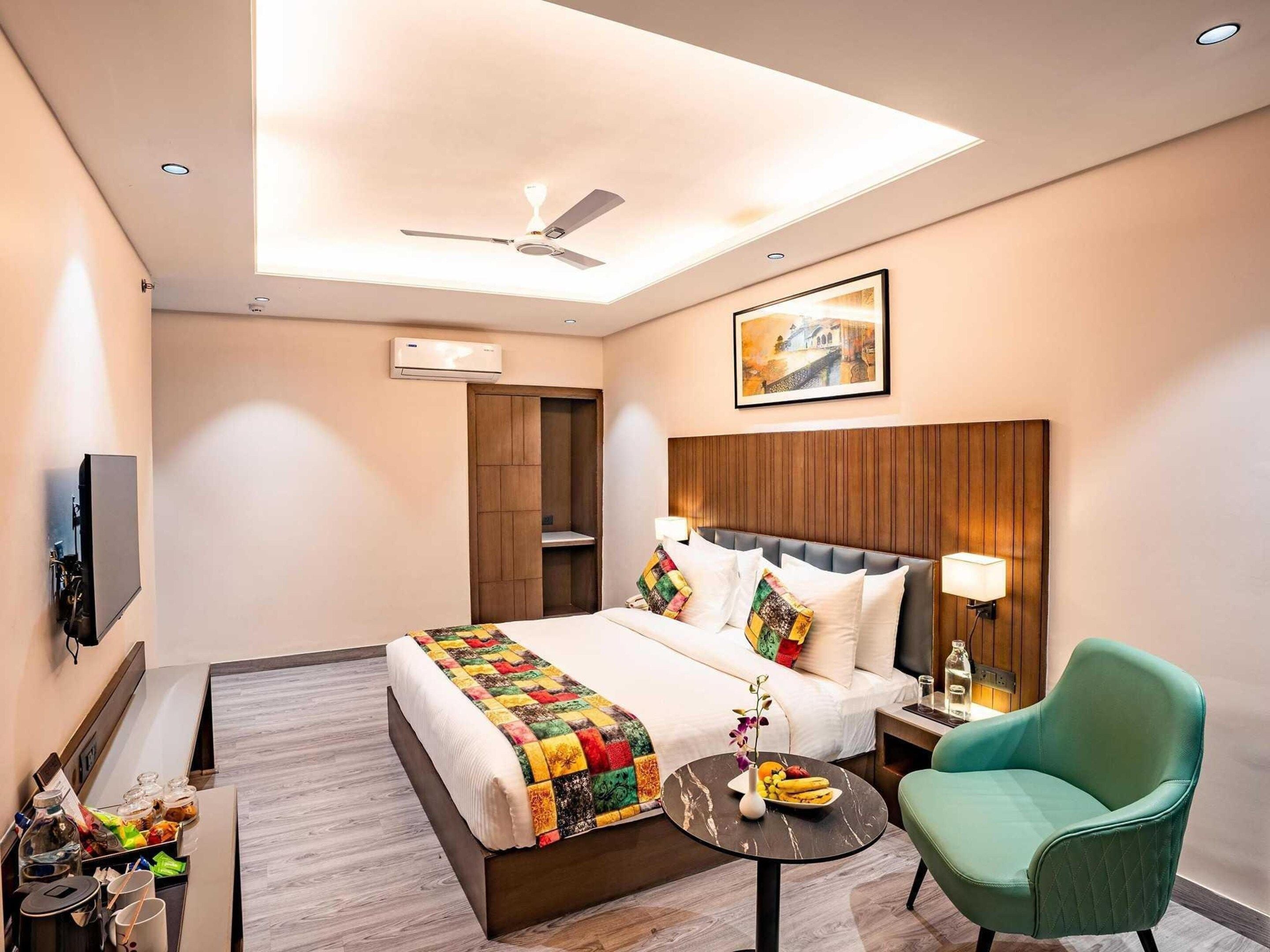 Een hotelkamer met een bed, een bureau, een stoel, een plafondventilator, een airconditioner en een schilderij aan de muur.