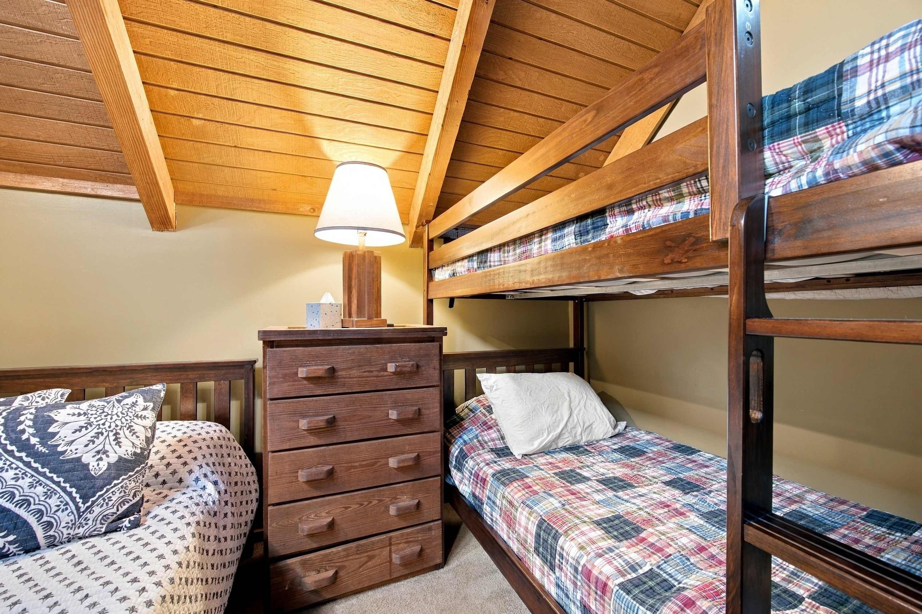 A bunk bed room with a wooden dresser and a lamp.