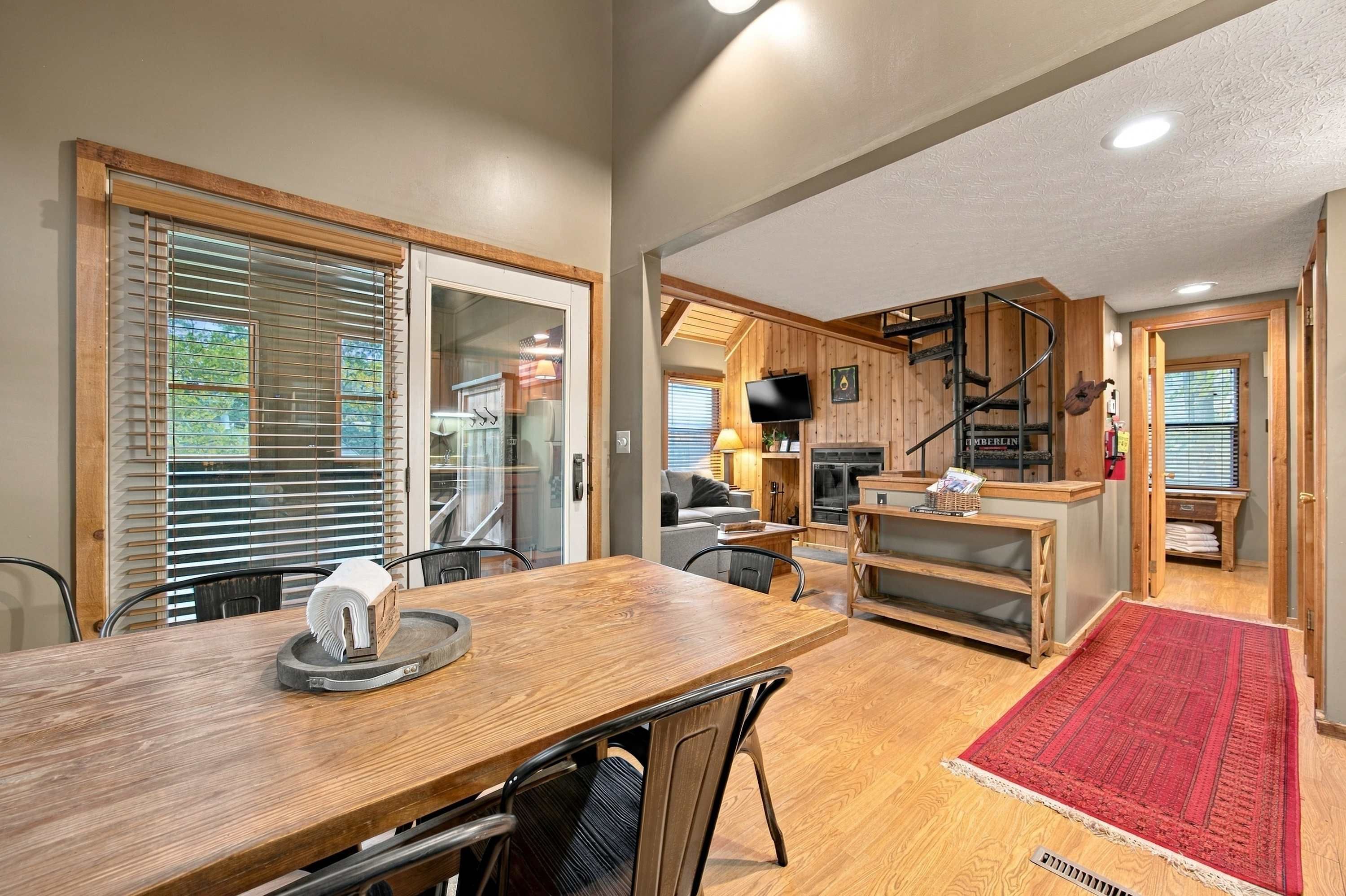 A modern kitchen with a wooden table and chairs, a TV mounted on the wall, and a staircase leading to a loft area.