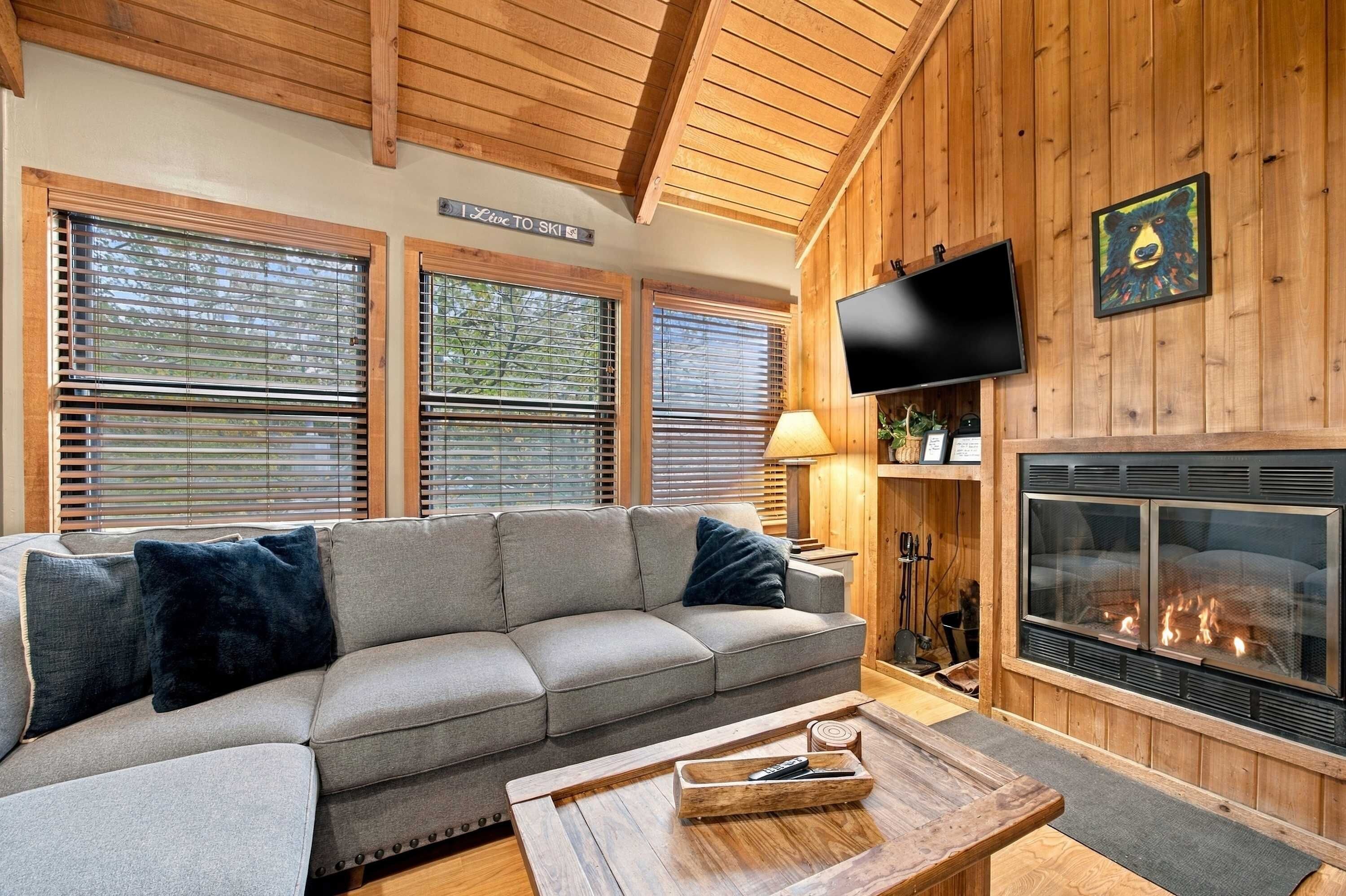 A cozy living room with a sectional sofa, a fireplace, and wooden walls.