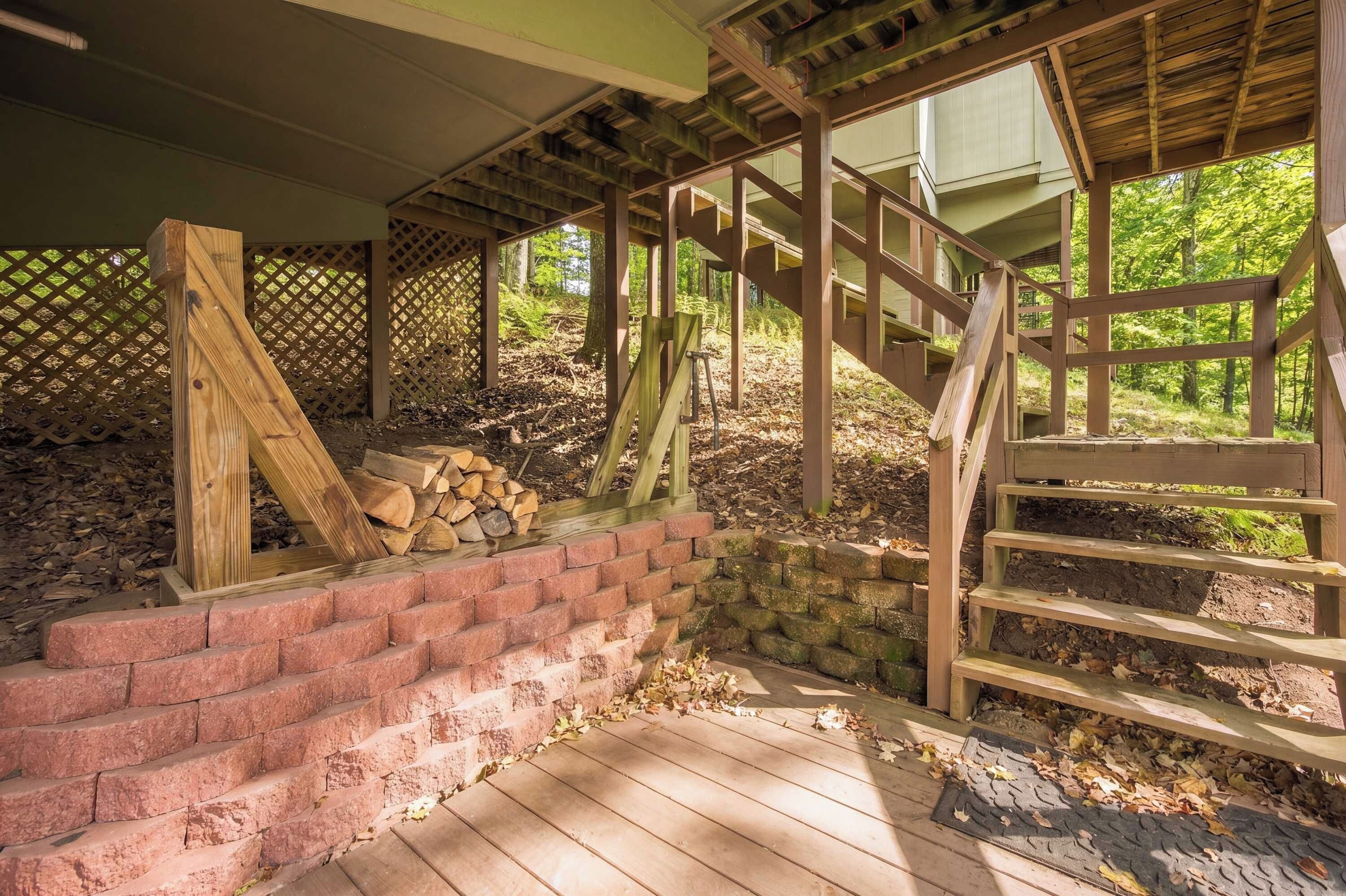 A wooden staircase leading up to a covered area with a wooden fence and a pile of firewood.
