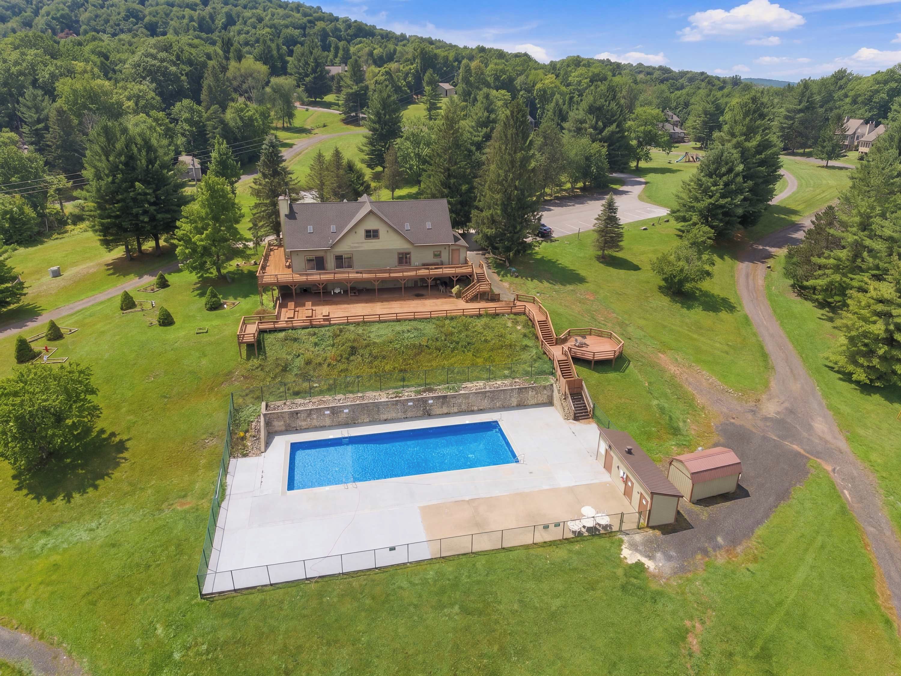 A large house with a swimming pool, surrounded by a well-maintained lawn and trees.