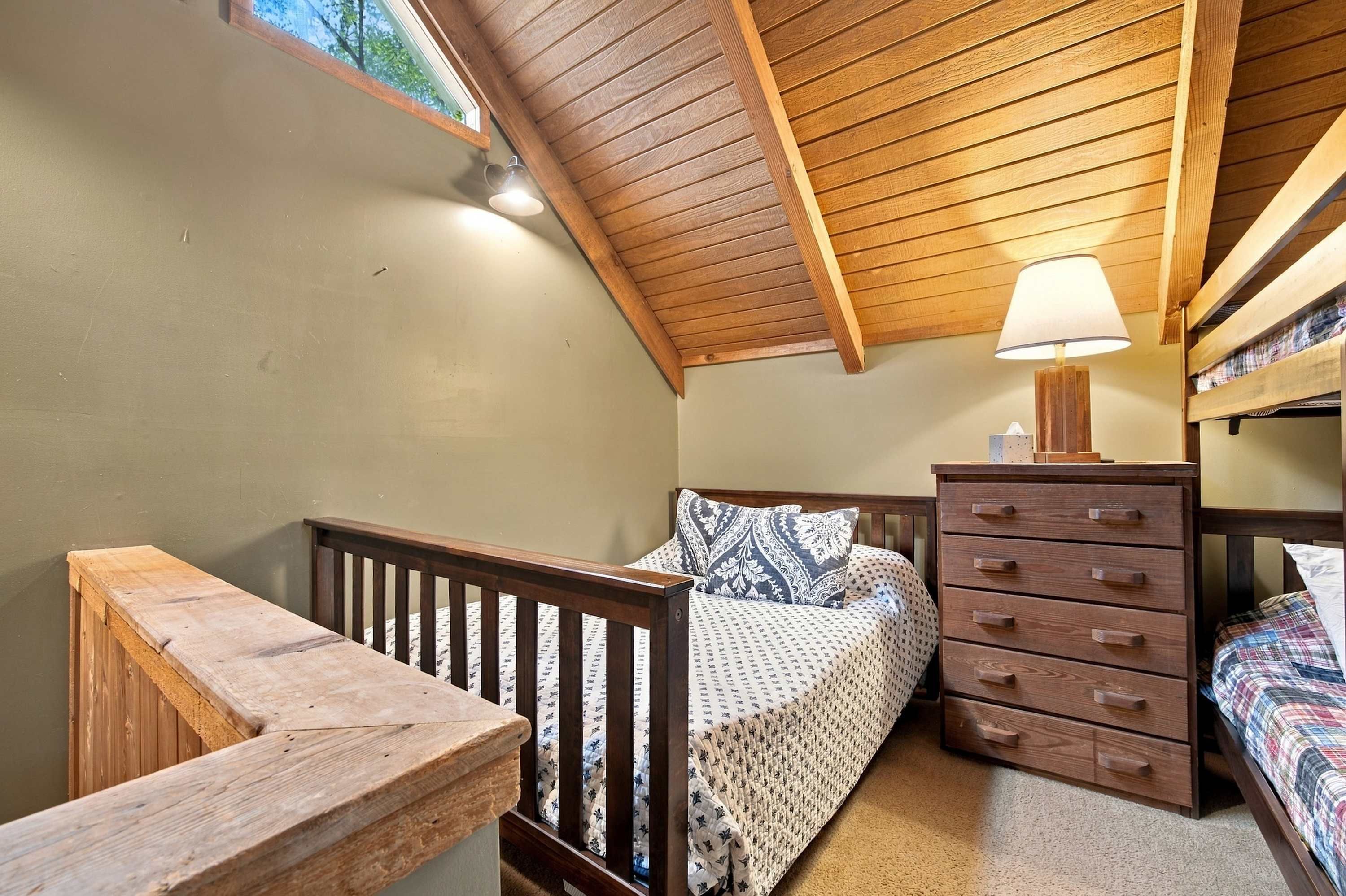 Une chambre avec un plafond en pente, un lit avec une literie à motifs, une commode et une table de chevet.
